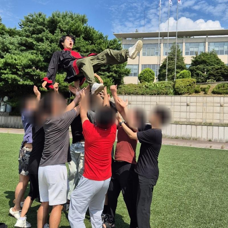 Isaac in a graduation gown, thrown into the air by friends on a sunny campus field. The others' faces are blurred.